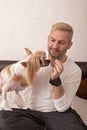 Middle aged smiling caucasian man in a white shirt is feeding his cute dog pet. Chinese crested, hairless puppy, hobby and Royalty Free Stock Photo