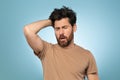 Middle aged tired and very sleepy man keeping hand on head and yawning, standing over blue studio background, free space Royalty Free Stock Photo