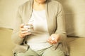 Middle aged unrecognized woman sitting at home, holding glas of fresh water and taking medicine.