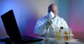 A middle-aged virologist is in the lab, sitting at a table with a laptop, flasks of tests on the table, examining Royalty Free Stock Photo