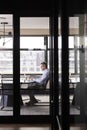 Middle aged white businessman working alone in a meeting room, seen through glass wall, vertical Royalty Free Stock Photo