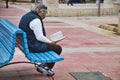 A middle-aged white Caucasian man sitting on a park bench reading a book