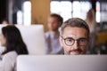 Middle aged white male creative using a computer in a busy office, selective focus, close up