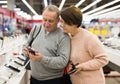 Middle aged wife and husband picking new smartphone in electronic store Royalty Free Stock Photo