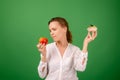 Middle-aged woman with apple and cake on a green background. Looks at the apple. The concept of choosing the right healthy food Royalty Free Stock Photo