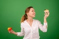 Middle-aged woman with apple and cake on a green background. Smiles and looks at the cake. The concept of choosing the right Royalty Free Stock Photo