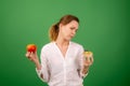 A middle-aged woman with an apple and a cake is tormented by her choice. On a green background. The concept of choosing the right Royalty Free Stock Photo