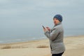 middle-aged woman on beach in autumn anxiously looks into the distance, holding a phone in her hands. adult woman on the