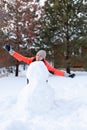 Middle aged woman with carrot in mouth standing behind unfinished snow man without head looking away in evening with