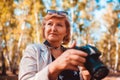 Middle-aged woman checking images on camera in autumn forest. Senior woman walking and enjoying hobby Royalty Free Stock Photo