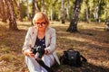 Middle-aged woman checking images on camera in autumn forest. Senior woman walking and enjoying hobby Royalty Free Stock Photo