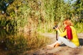 Middle-aged woman checking images on camera sitting by autumn river bank. Senior woman enjoying hobby Royalty Free Stock Photo