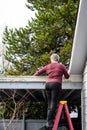 Middle aged woman climbing a ladder to a carport flat roof for storm debris cleanup