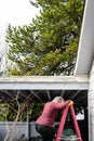 Middle aged woman climbing a ladder to a carport flat roof for storm debris cleanup