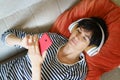 Woman consulting her smartphone while listening to music with headphones lying on the sofa.