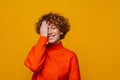 Middle-aged woman covering her face while standing isolated over yellow backkground