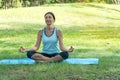 Middle-aged woman doing Yoga in the parks. Female standing on Yoga mat on the grass in the park exercises outdoors. Royalty Free Stock Photo