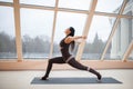 Middle aged woman doing yoga in Virabhadrasana One or Warrior One yoga pose on the mat in front of large windows., exercise fitnes Royalty Free Stock Photo