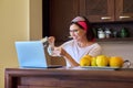 Middle aged woman drinking coffee talking on video call using laptop, kitchen at home Royalty Free Stock Photo