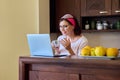 Middle aged woman drinking coffee talking on video call using laptop, kitchen at home Royalty Free Stock Photo