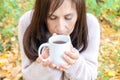 Middle-aged woman eyes closed with pleasure holding mug of hot tea in a hand in the autumn forest. close-up