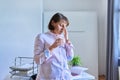 Middle aged woman with a glass of water suffering from headache in home office Royalty Free Stock Photo