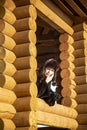 A middle-aged woman in a hat looks out of the window of a log house Royalty Free Stock Photo