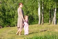 Middle aged woman holding hands with little girl in summer park with trees looking aside Royalty Free Stock Photo