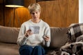 Middle-aged woman holds a package of pills and reads medical instructions sitting on the couch Royalty Free Stock Photo