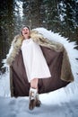 A middle-aged woman in a large warm fur coat and white angel wings in a winter forest with snow and snowdrifts. Fairy angel in a Royalty Free Stock Photo