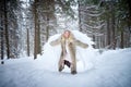 A middle-aged woman in a large warm fur coat and white angel wings in a winter forest with snow and snowdrifts. Fairy angel in a Royalty Free Stock Photo