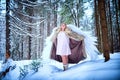 A middle-aged woman in a large warm fur coat and white angel wings in a winter forest with snow and snowdrifts. Fairy angel in a Royalty Free Stock Photo