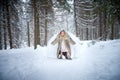 A middle-aged woman in a large warm fur coat and white angel wings in a winter forest with snow and snowdrifts. Fairy angel in a Royalty Free Stock Photo