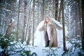A middle-aged woman in a large warm fur coat and white angel wings in a winter forest with snow and snowdrifts. Fairy angel in a Royalty Free Stock Photo