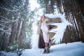 A middle-aged woman in a large warm fur coat and white angel wings in a winter forest with snow and snowdrifts. Fairy angel in a Royalty Free Stock Photo