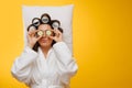 Housewife on pillow with hair in rollers holding cucumber slices over her eyes Royalty Free Stock Photo