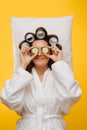 Woman lies on pillow with hair in rollers holding cucumber slices over her eyes Royalty Free Stock Photo