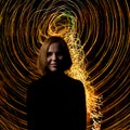 A middle-aged woman looks at the camera against a background of bright traces of moving light at a long exposure