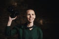 A middle-aged woman photographer holding a camera, smiling, and facing the camera against a dark background Royalty Free Stock Photo