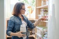 Middle-aged woman picking food from storage cabinet in kitchen Royalty Free Stock Photo