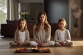 Middle-aged woman practising relaxing yoga at home with her joyful daughters. Bright daylight photo.