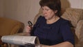 Middle-aged woman reads a newspaper through a magnifying glass sitting in a chair Royalty Free Stock Photo