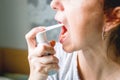 Middle-aged woman. With red hair. With a tired, sickly face. Sprays a spray for sore throat. On a gray background Royalty Free Stock Photo