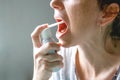 Middle-aged woman. With red hair. With a tired, sickly face. Sprays a spray for sore throat. On a gray background Royalty Free Stock Photo