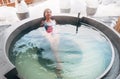 Middle-aged woman relaxing in Hot water jacuzzi outdoor bathtub in winter forest wellness hotel and enjoying pleasant healthy body