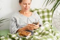 A middle-aged woman remains in bed, absorbed in her phone screen all day. Mental decline, sloth, inactivity