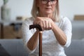 Middle-aged woman seated on couch holding in hands cane