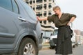 Middle aged woman with short hair standing by a parked car and looks at bumper damage