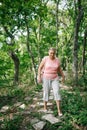 Middle aged woman singly walk along fenced stone path looking at feet in green forest. Tourist with interest go through