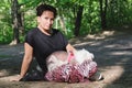 Middle-aged woman sits on a path in a park with a Chinese Crested dog on her lap